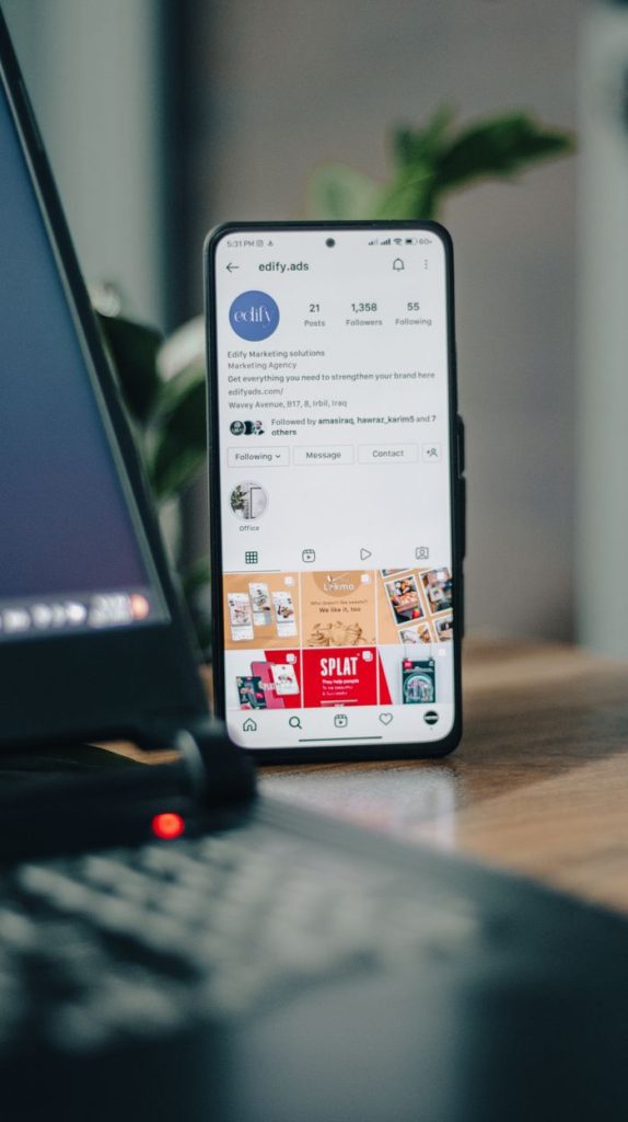 Vertical shot of a smartphone displaying an Instagram profile next to a laptop, representing social media engagement.